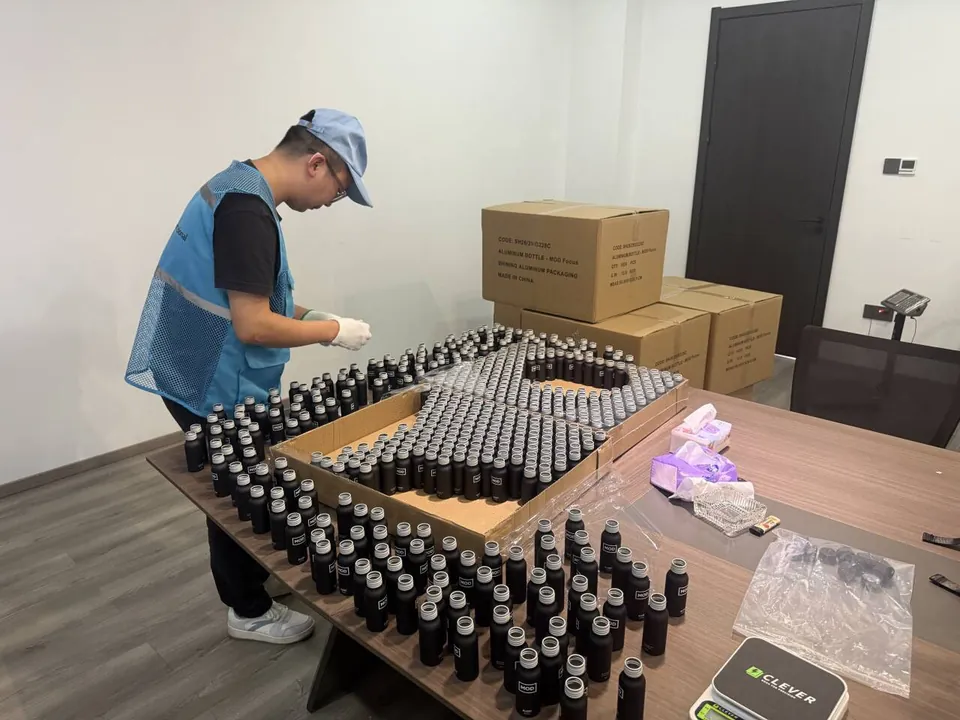장갑을 낀 SSTI 검사원이 테이블에 펼쳐 놓은 작은 병들을 디지털 저울과 함께 검사하는 모습
